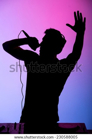 Portrait of a young DJ at work with a microphone on the colored background.