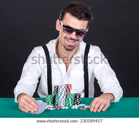 The poker player in black glasses, in a casino. Gambling chips and cards, green table. On a black background.