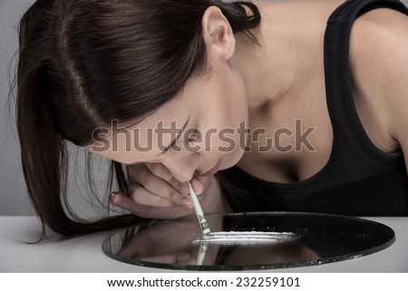 Addicted young woman is sniffing lines of drugs.