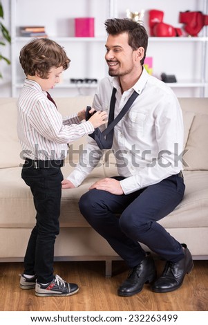 Little son is tying necktie to dad. Father is going to go to work.