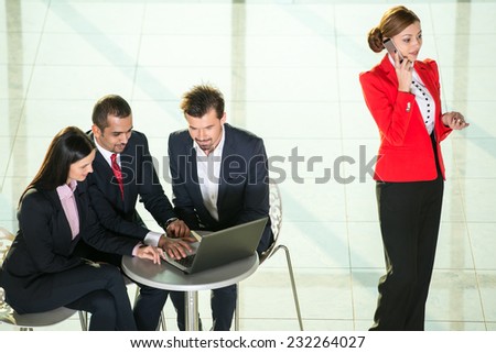 Portrait of several business people are looking at laptop. Their colleague is talking by phone.