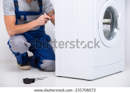 Repairman is repairing a washing machine on the white background.