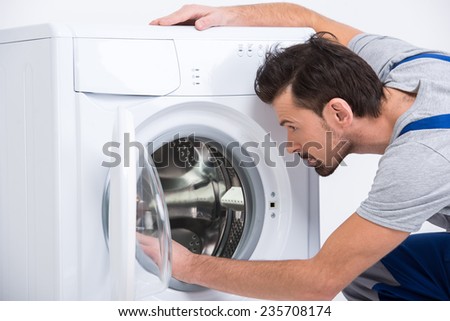 Repairman is repairing a washing machine on the white background.