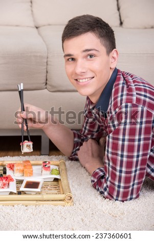 Young smiling man with sushi on the floor at home. He is looking at the camera.