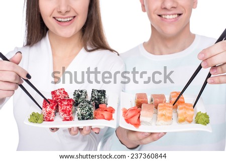 Eating sushi together. Beautiful couple are eating sushi while standing on white background.