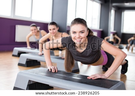 Fitness, sport, training, gym and lifestyle concept. Three young women are working out with steppers in gym.