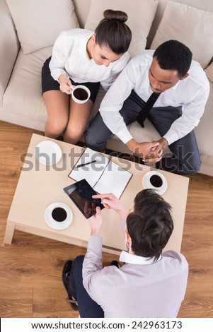 Top view of three business people are sitting at the table and discussing something with coffee.