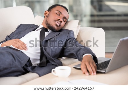 Young African business man is holding hand on laptop keyboard while sleeping on the couch.