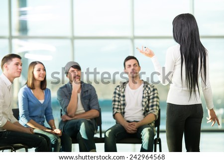 Young woman is sharing her problems with people. View of woman is telling something and gesturing while group of people are sitting in front of her and listening.