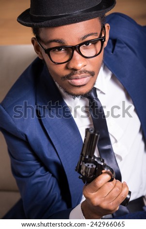 Young black man is wearing suit and hat with gun.