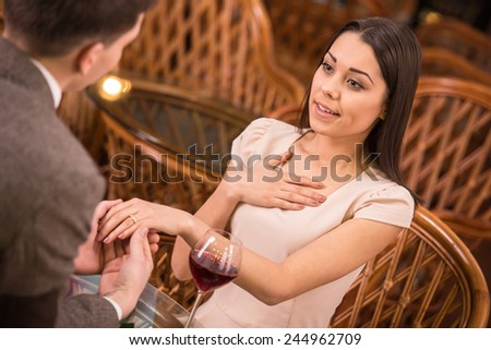 A man is giving a ring as a gift to a female in an outdoor cafe.