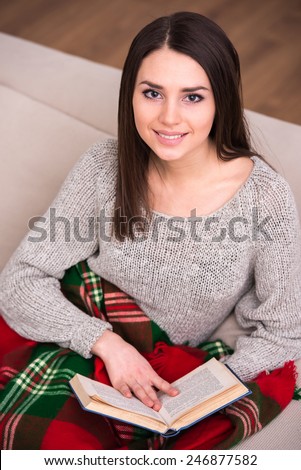 Beautiful young girl sitting on sofa at home wrapped a blanket and is reading.