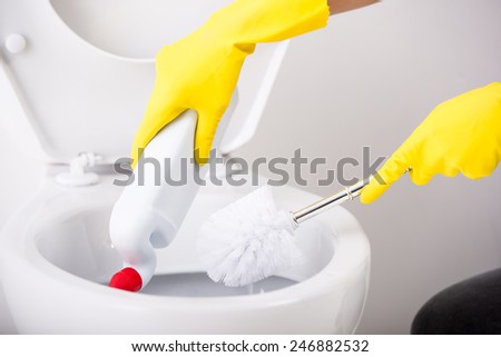 Female hand in yellow rubber glove is cleaning toilet bowl using brush.