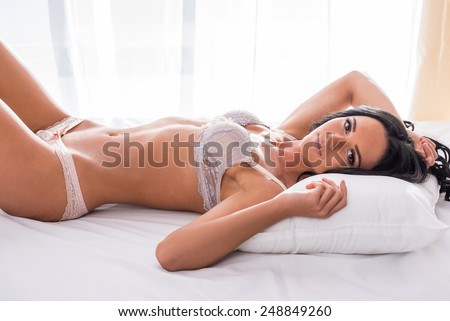 Side view of beautiful young woman with perfect body  is lying on bed.