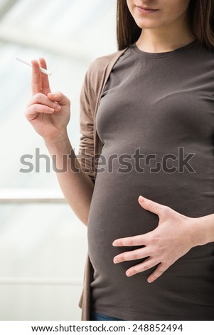 Young pregnant is holding a cigarette. Unhealthy. Pregnant woman is smoking.