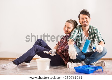 Tired young couple are sitting on the floor with paint brush and bucket  while doing repair at home.