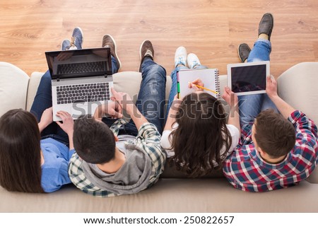 Top view of a four young people, students are sitting on sofa with laptop and tablet, are studying.