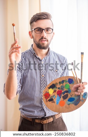 Portrait of a young male artist is holding a brush and mix color oil painting on palette.