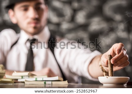 Confident gangster man is smoking a cuban cigar. A lot of money is on the table.