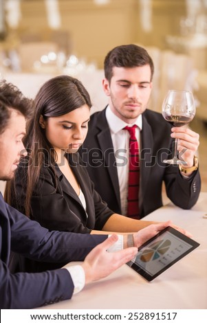 Three business partners are looking at the pc tablet while sitting at a restaurant.