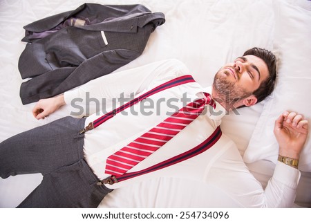 Top view of young handsome man is sleeping on bed in suit.
