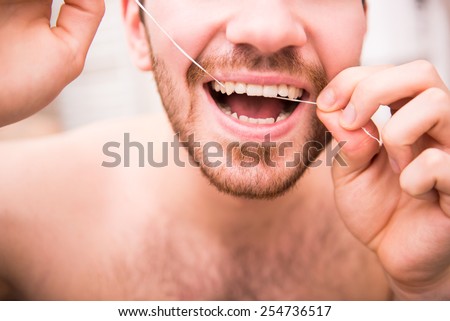Close-up of young man is cleaning teeth with dental floss.