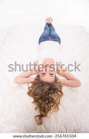 Young, smiling woman is lying on the quality mattress over white background.
