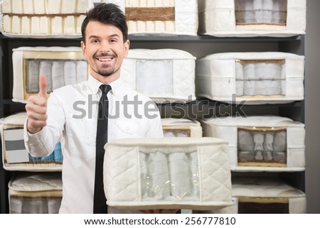 The young salesman is showing quality mattresses in the store.