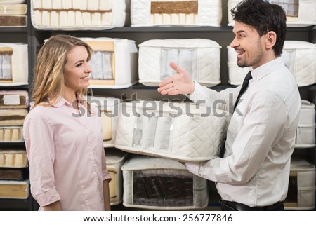 Good choice. The young salesman tells the customer about quality mattresses in the store.