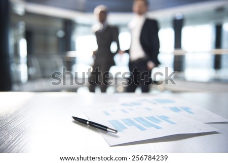 Focus on documents and pen on the table. Blurred people on background.