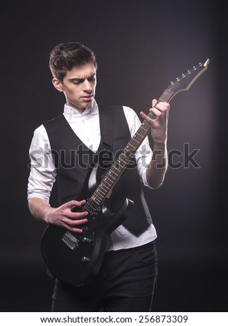 Young male musician is playing a six-string bass guitar isolated on dark background.