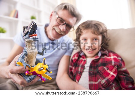 A preschooler and his grandpa happily are playing with toy dinosaurs.