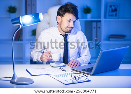 Confident man is working on laptop in office and drinking a coffee