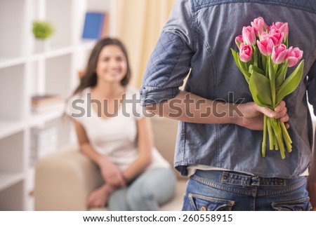 Guy is holding flower behind him is trying to surprise his is waiting girlfriend at home.