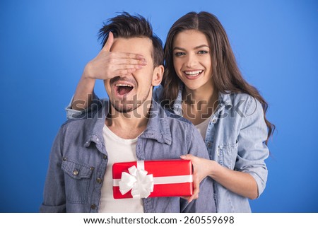 Girl is giving a gift to her boyfriend. Isolated on blue background.