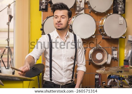 Young attractive man is playing the drums in the music store.