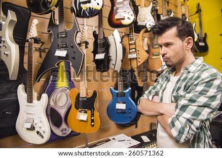 Young man is considering electric guitars music store.