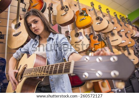 Beautiful young girl is playing guitar in a music store.