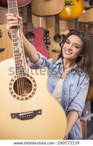 Beautiful young girl is holding a guitar in music store.