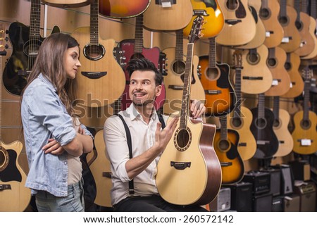 Man is showing to girl guitar in a music store.