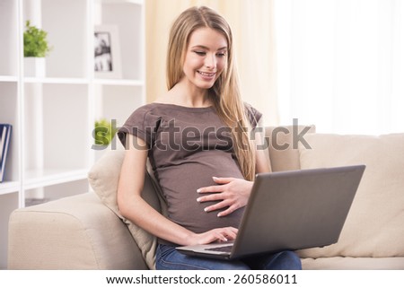 Beautiful pregnant woman is working on laptop and sits on couch.