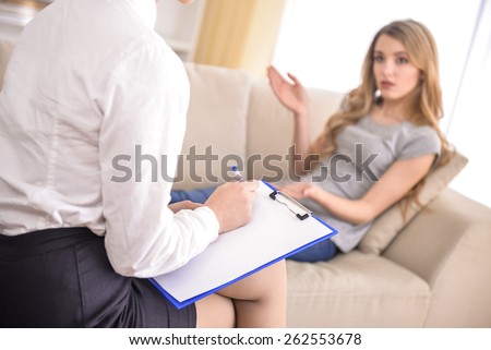 Psychologist talking with woman on the couch and taking notes in therapists office.