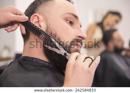 Hairdresser shaving  with scissors and combs ofclient in professional hairdressing salon.