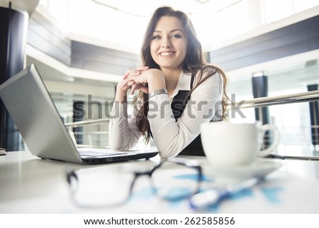 Smiling young business woman working for a laptop in a modern office.