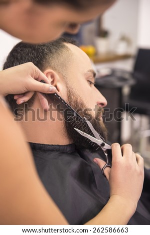 Side view of hairdresser shaving  with scissors and combs of satisfied client in professional hairdressing salon.