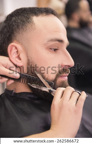 Hairdresser shaving  with scissors and combs of satisfied client in professional hairdressing salon.