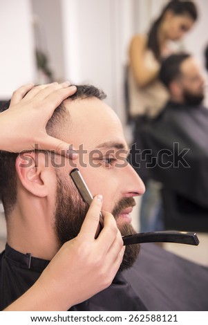 Hairdresser shaving an old-fashioned razor of satisfied client in professional hairdressing salon.