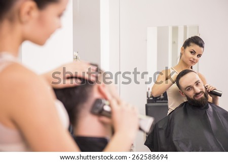 Hairdresser cuts hair with hair clipper on back of the head  of handsome satisfied client   in hairdressing salon.