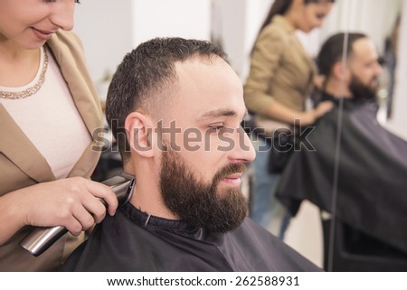 Hairdresser cuting hair with hair clipper on back of the head  in hairdressing salon