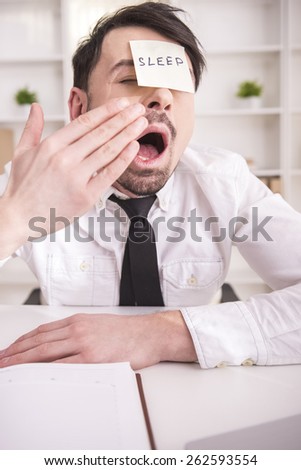 Close-up exhausted young businessman is yawning at work in office.